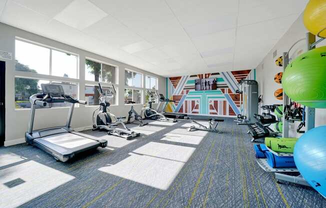 a gym with treadmills and weights in a room with windows at Sunnymead Apts Apartments, Moreno Valley