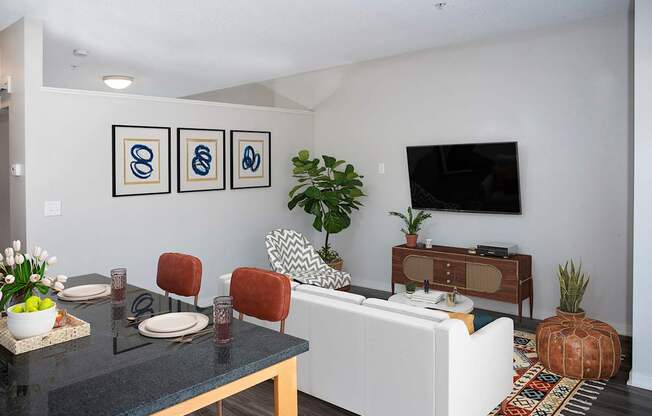 A modern living room with a white sofa, a black coffee table, and a TV on the wall.