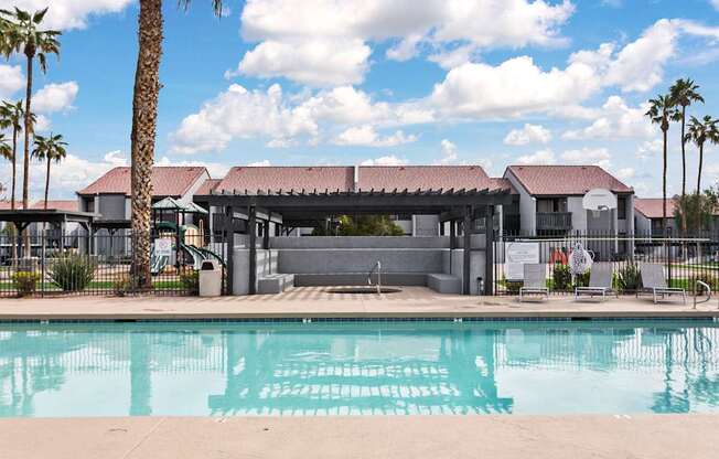 A pool in front of a building with a fence and palm trees.