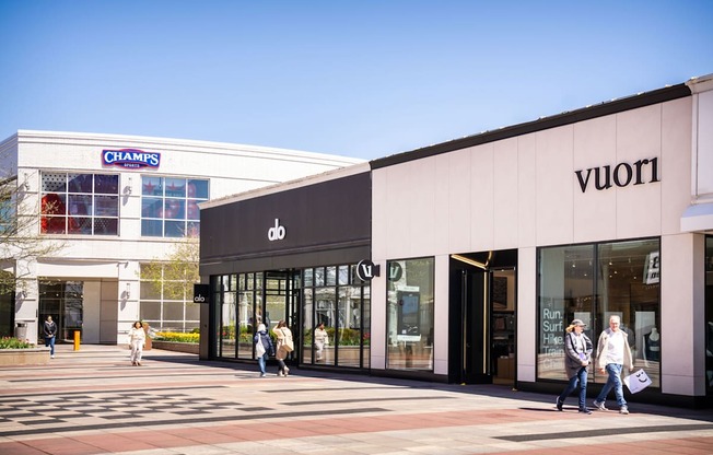 A street view of a Champs and a Vuori store with people walking by.