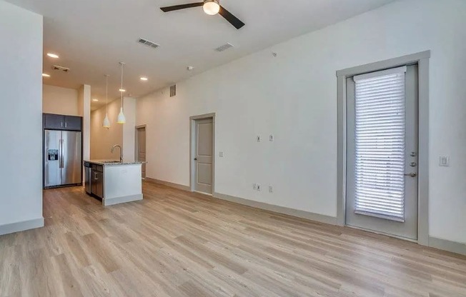 an empty living room with a kitchen and a ceiling fan