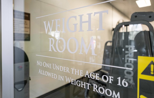 a weight room sign on the door of a gym with escalators