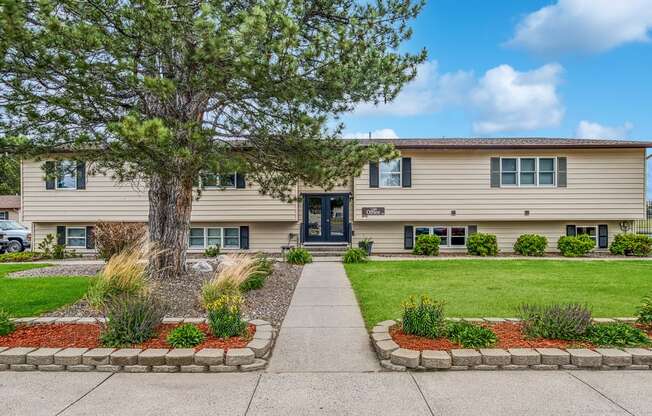 a beige house with a tree and a sidewalk in front of it