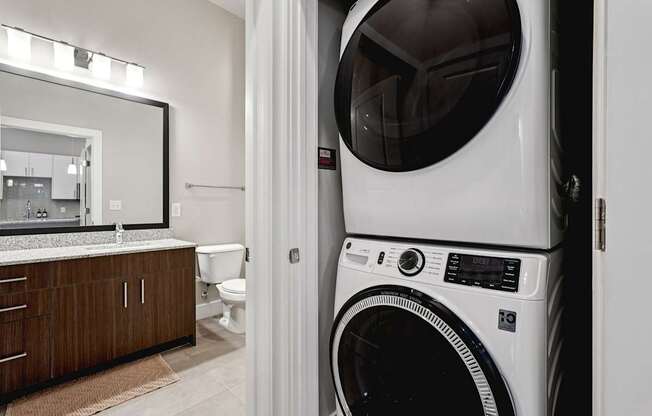 A full sized, white washing and drying machines  closet, with a view of the bathroom in the background.