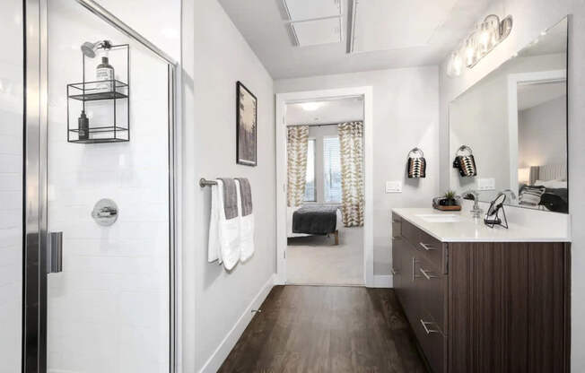 A bathroom with a white tile shower, a wooden vanity, and a large mirror.