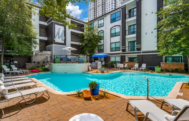 a swimming pool with chairs and umbrellas in front of an apartment building