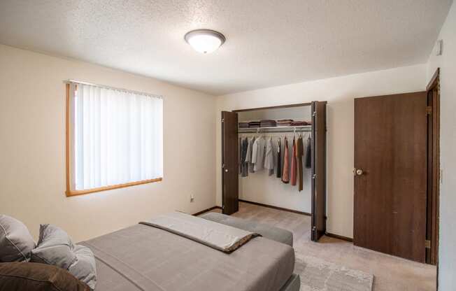 A bedroom with a bed and a closet with clothes in it. Bismarck, ND Eastbrook Apartments.