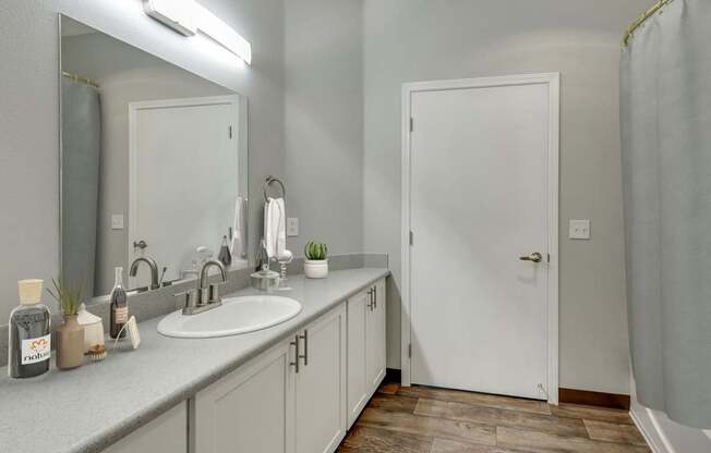 Model Bathroom with White Cabinets, Wood-Style Flooring and Shower/Tub at Landings at Morrison Apartments located in Gresham, OR.