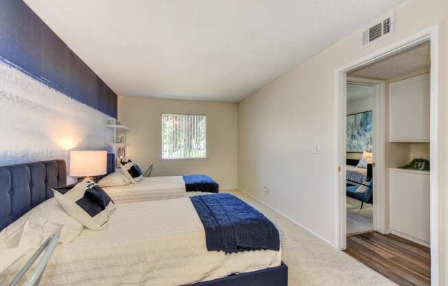 Bedroom with 2 twin beds with blue and white bedding.  Washer and dryer visible in hallway at Renaissance Park Apartments, Davis, California