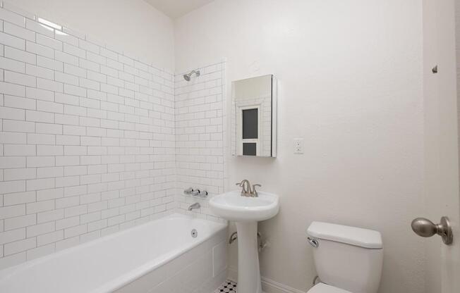 A white bathroom with a tub, toilet, and sink at Westmore Manor Apartments, Los Angeles, California