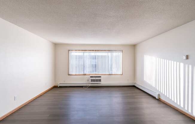 an empty living room with a large window and wood floors. Fargo, ND North Manor Apartments