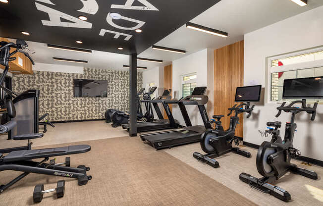 A gym with a variety of exercise equipment including treadmills, stationary bikes, and dumbbells.