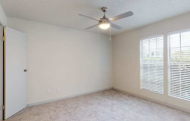 an empty bedroom with a ceiling fan and large windows