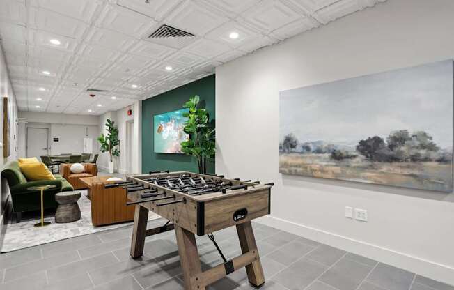A room with a green chair, a wooden table, and a painting on the wall.
