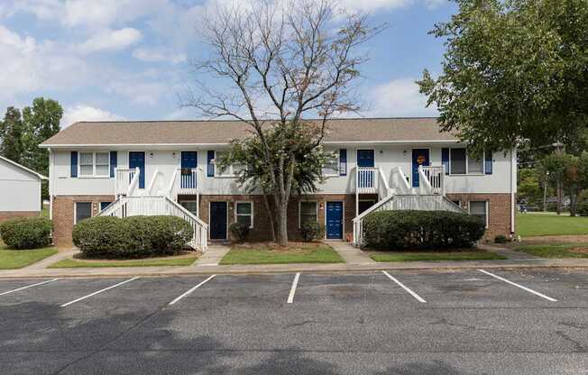 A parking lot in front of a building with a tree in the middle.