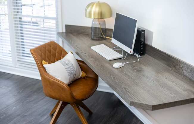 A brown chair with a white pillow sits in front of a desk with a computer.