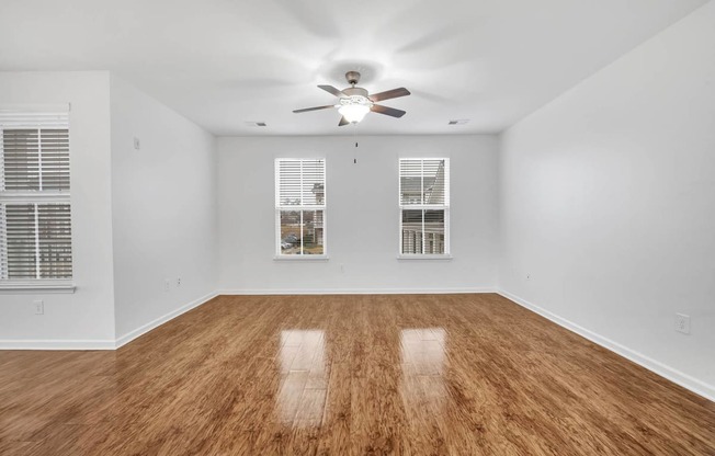 an empty living room with a ceiling fan and windows