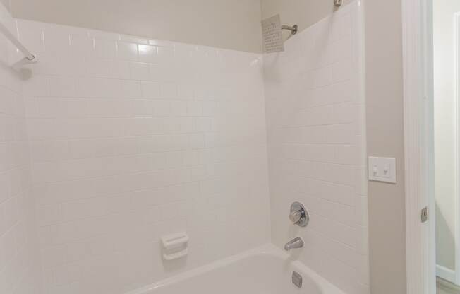 A white tiled shower with a white tub and a white shower head.