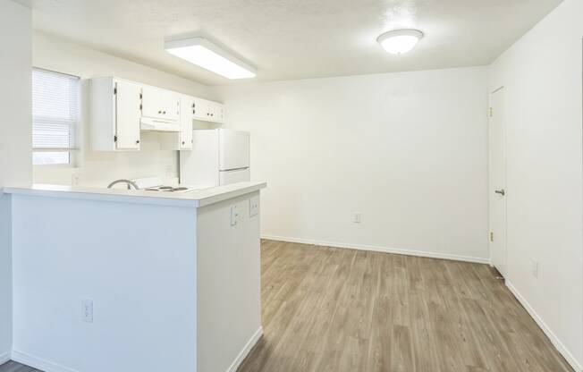 an empty kitchen and living room with white cabinets and wood flooring
