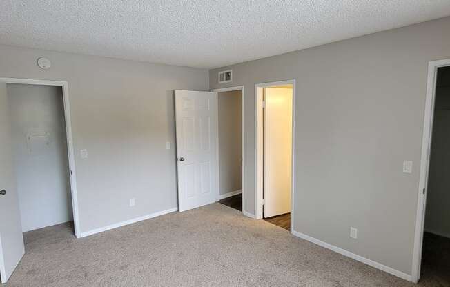 Carpeted master bedroom with two walk-in closets and shared bathroom at La Mesa Village Apartments in La Mesa, California.