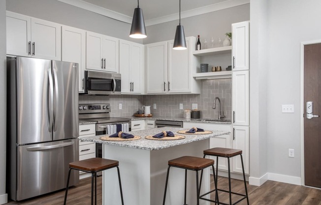 a kitchen with stainless steel appliances and a island with three stools at The Edison at Maple Grove, Maple Grove, MN