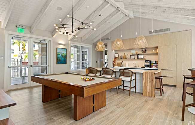 A billiard table is in the middle of a room with a kitchen area in the background.