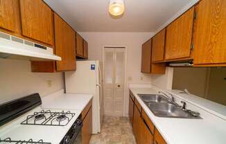 A kitchen with a gas stove and wooden cabinets at Trappers Cove Apartments, Lansing