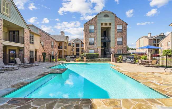 Swimming pool surrounded by apartment buildings with lounge chairs at Bandera Crossing apartments in San Antonio, TX