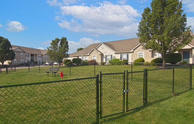 A black fence surrounds a green field with houses in the background.