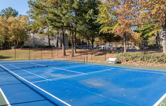 A blue tennis court surrounded by trees and a fence.