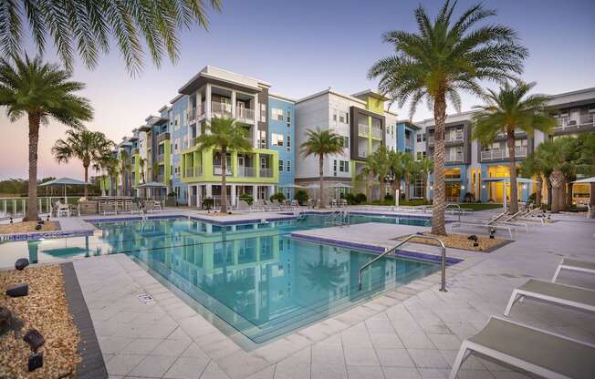 The swimming pool and large pool deck with towering palms and apartment homes at Residences at The Green in Lakewood Ranch