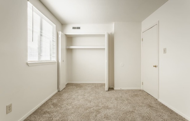 a bedroom with white walls and carpet and a closet