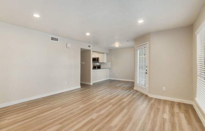 an empty living room with a kitchen in the background