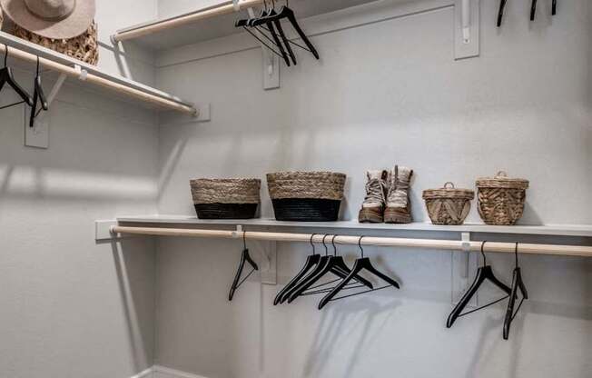 A white closet with clothes hanging and baskets on the shelf.