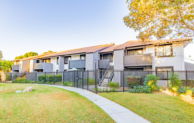 A modern apartment building with a black fence and a sidewalk.