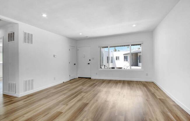 a living room with white walls and a large window and wooden floors