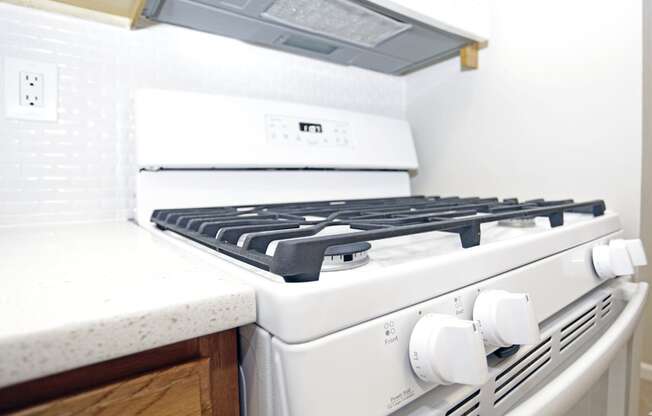 A white gas stove with a white countertop and a white wall in the background.