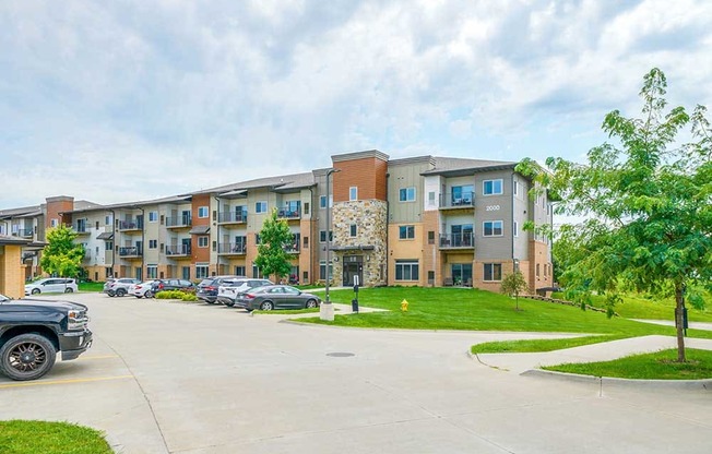 A modern stone and brok apartment building with grassy lawns, and a large parking lot.