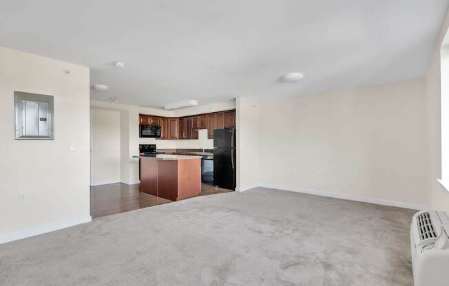 an empty living room with a kitchen in the corner