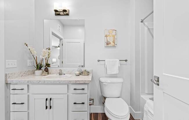 A white bathroom with a marble counter top and a toilet.