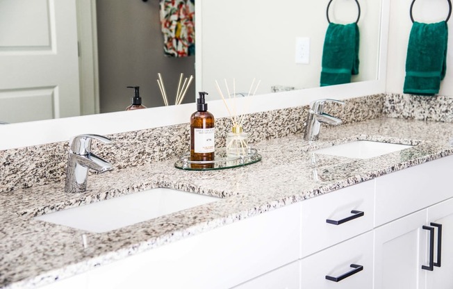 En suite bathroom vanity with granite countertops, stain-resistant plank flooring, and a double sink seamlessly connecting to the luxurious master bedroom.