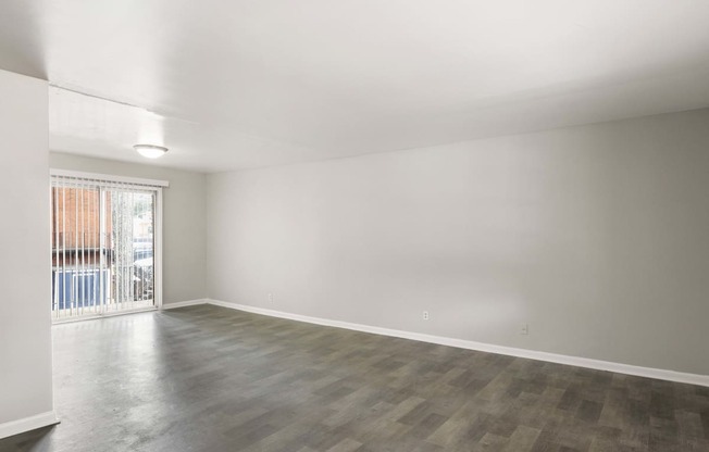 an empty living room with a sliding glass door to a balcony