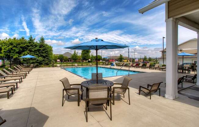 a swimming pool with a table and chairs under an umbrella at The Winhall of Williams Pointe Apartments, IOWA