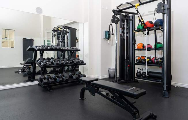 A black weight bench in a room with a mirror and a rack of weights.
