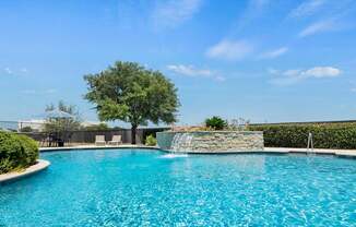 A pool with a waterfall and a tree in the background.