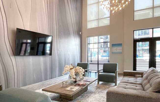 A living room with a grey couch, a coffee table, and a large flat screen TV mounted on the wall.