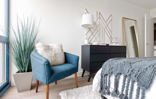 a bedroom with a bed and a blue chair and a black dresser