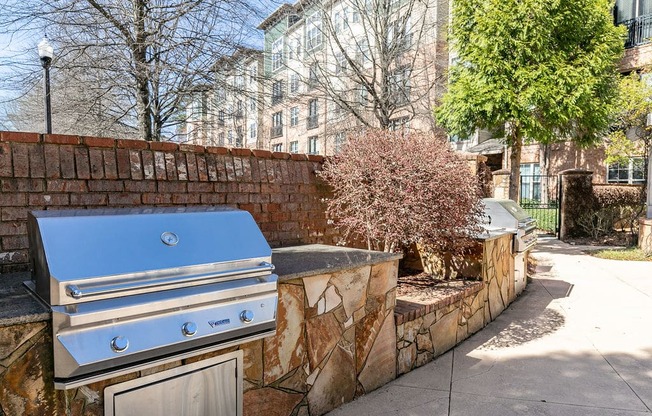 an outdoor kitchen with a grill and a tree in front of a brick wall