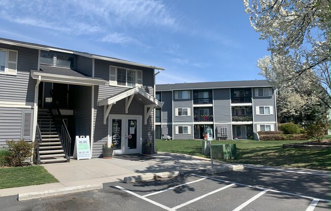 a gray apartment building with a lawn and trees in front of it