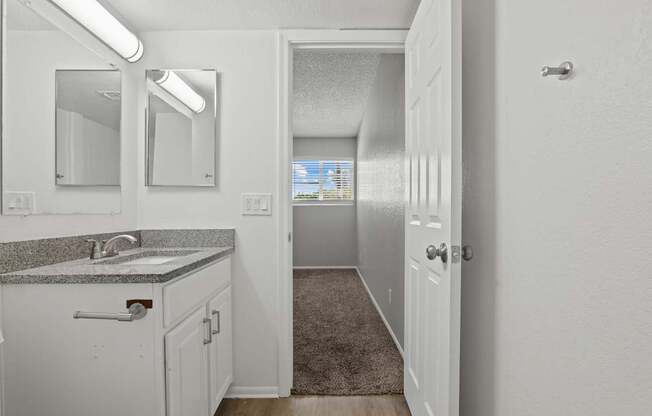 A bathroom with a sink, mirror, and a door leading to another room.